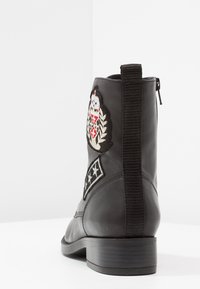 Musta nahkasaapas nilkkamallilla, jossa on brodeeratut yksityiskohdat, elastinen sivupaneeli ja matala lohkokorko; sileä pinta ja pyöreä kärki.