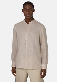 Camicia beige a maniche lunghe con colletto a bande, tessuto di lino leggero e chiusura con bottoni; presenta un orlo leggermente curvo e una vestibilità su misura.