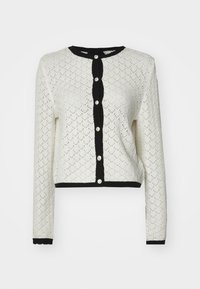 Cardigan alb din dantelă tricotată, cu mâneci lungi și un design scurt. Accente negre plisate de-a lungul gâtului, a butonierelor și la tiv. Cinci nasturi.