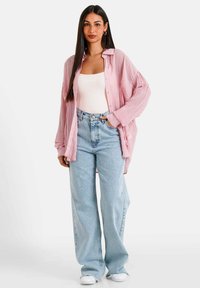 Camisa de botones de color rosa claro con textura acanalada, combinada con pantalones de mezclilla de pierna ancha de cintura alta en un azul claro y zapatillas blancas.