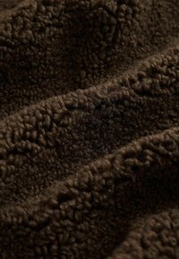 Närbild av mörkbrunt mjukt fleecetyg med texturerad, fluffig yta och vågiga veck.