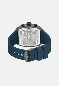 Vierkante roestvrijstalen horloge met een blauwe rubberen band. Heeft een zilveren wijzerplaat met een radiaal patroon en "POLICE" branding. Twee zwarte knoppen aan de bovenkant.