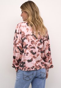 Majica dugih rukava, labavog kroja, u uzorku ružičaste i smeđe tye-dye boje, napravljena od mekog materijala; uparena s plavim farmerkama s džepovima.