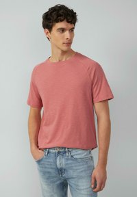 T-shirt z krótkim rękawem, okrągłym dekoltem w jasnoróżowym, fakturowanym materiale. Luźny krój z rękawami raglanowymi, zestawiony z jasnoniebieskimi dżinsami.