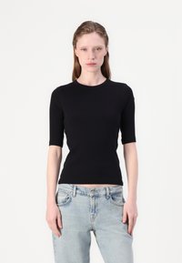Sort kortærmet tætsiddende top lavet af glat materiale, med en rund halsudskæring, parret med lyse vaske, løstsiddende jeans.