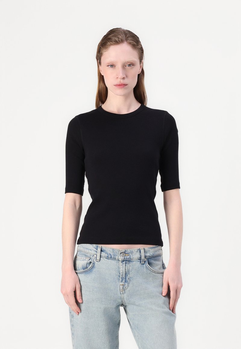 Sort kortærmet tætsiddende top lavet af glat materiale, med en rund halsudskæring, parret med lyse vaske, løstsiddende jeans.