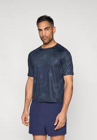 Tengerészkék rövid ujjú sportpóló texturált, elmosódott mintával. Kerek nyakkivágással és raglán ujjakkal rendelkezik. Aktív viseletre alkalmas.