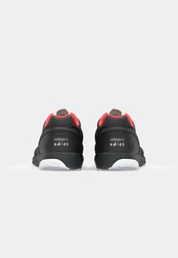 Black running shoes with red accents, featuring a cushioned heel, textured rubber sole, and white branding on the heel and side.