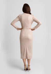 Długa, dopasowana sukienka z jasnego beżowego materiału z subtelnym połyskiem. Posiada długie rękawy, szwy z tyłu oraz długość do kolan. Noszona z beżowymi szpilkami.