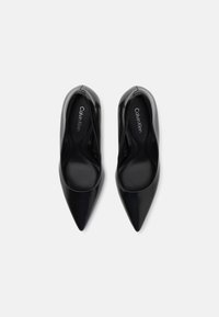 Escarpins noirs à bout pointu avec une finition laquée lisse, présentant un design minimaliste et une semelle intérieure de marque Calvin Klein.