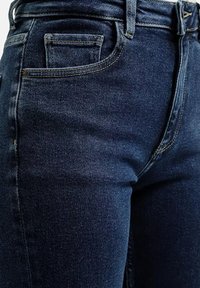Granatowe dżinsy o gładkiej strukturze, z standardowymi kieszeniami, szlufkami na pasek i kontrastującymi szwami wzdłuż krawędzi.