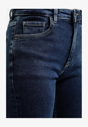 Granatowe dżinsy o gładkiej strukturze, z standardowymi kieszeniami, szlufkami na pasek i kontrastującymi szwami wzdłuż krawędzi.