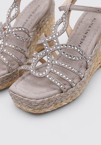 Sandalias de cuña de esparto grises con adornos de strass, correas de ante y una plataforma de yute trenzado. Presenta una cama para los dedos plana y un diseño intrincado.