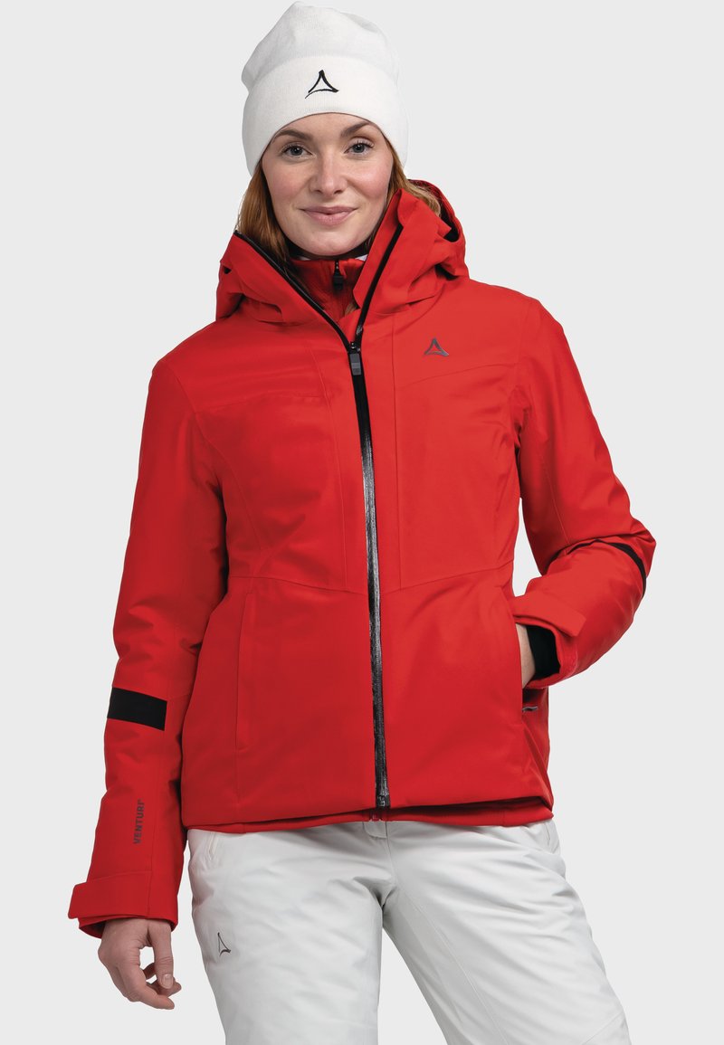Rote wasserdichte Jacke mit Kapuze, schwarzen Akzenten, Reißverschlüssen und Logo. Kombiniert mit weißen isolierten Hosen. Leicht und mit glatter Textur.