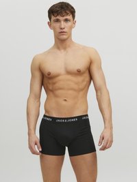 Schwarze Baumwollboxershorts mit einem markierten Bund, bieten eine enge Passform und eine glatte Textur. Das Modell steht mit einem neutralen Gesichtsausdruck.