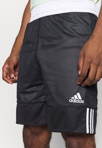 Pantalones cortos deportivos negros con rayas blancas y el logo de Adidas. Fabricados con tejido de malla transpirable, cuentan con una cintura elástica y una superficie texturizada.