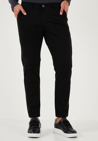 Pantaloni negri din bumbac cu croi slim și o textură netedă. Dispun de închidere cu un buton în față și fermoar, precum și două buzunare laterale.