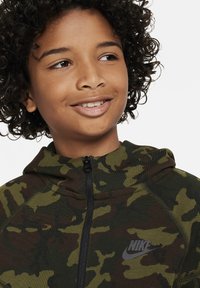 Felpa con zip verde camouflage e colletto alto, dotata di un logo Nike in gomma nera sul petto e una robusta chiusura a zip.