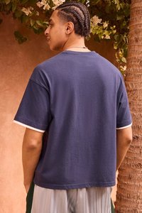 Marineblaues Baumwoll-T-Shirt mit lockerem Schnitt, weißen Abschlüssen an den Ärmeln, unifarbenem Rücken und kurzen Ärmeln. Strukturierter Stoff.