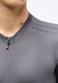 Κοντινό πλάνο ενός ατόμου που φοράει γκρι ποδηλατική φανέλα Castelli με εμπρόσθιο φερμουάρ και υφασμένο ύφασμα.