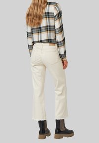 Jeans bianchi a vita alta con orlo sfrangiato, abbinati a una camicia a quadri bianca e nera. Stivali neri alla caviglia con suola spessa e dettagli in rete.