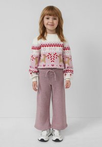Helles rosa festliches Sweatshirt mit Rentieren und Zuckerstangen, kombiniert mit flauschigen, lockeren lavendelfarbenen Hosen und weißen Sneakers.