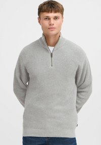 Suéter de cuello con cremallera en gris claro, con un patrón de tejido texturizado, mangas acanaladas y cinturilla. Presenta una cremallera corta en el cuello.