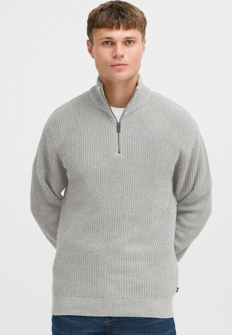 Suéter de cuello con cremallera en gris claro, con un patrón de tejido texturizado, mangas acanaladas y cinturilla. Presenta una cremallera corta en el cuello.