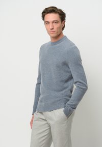 Helles blaues Rundhals-Sweatshirt aus weichem Strickmaterial, mit langen Ärmeln und gerippten Bündchen, kombiniert mit hellgrauen maßgeschneiderten Hosen.