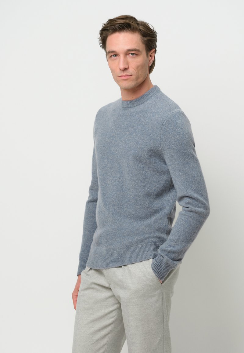 Helles blaues Rundhals-Sweatshirt aus weichem Strickmaterial, mit langen Ärmeln und gerippten Bündchen, kombiniert mit hellgrauen maßgeschneiderten Hosen.