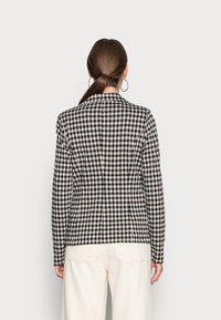 Veste à carreaux noir et blanc au design ajusté, tissu texturé, revers en pointe et fente simple au dos, associée à un pantalon de couleur crème.