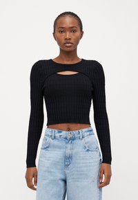 Must mustriba crop-top pikendatud varrukatega, mille kaeluses on auk. Kombineeritud helesiniste kõrge vöökohaga teksadega.