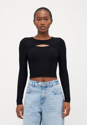 Crop top noir à rayures avec des manches longues, comportant une découpe en forme de clé au niveau du col. Associé à un jean taille haute bleu clair.