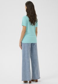 Světle modré bavlněné tričko s krátkým rukávem, kombinované s džínami s vysokým pasem a širokými nohavicemi, které mají světlejší praní a nedokončený lem.