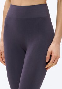 Κολάν υψηλής μέσης, ελαστικό, σε σκούρο μωβ χρώμα. Ομαλό ύφασμα με διακριτική υφή, με λογότυπο στη μέση. Εφαρμοστή σχεδίαση.