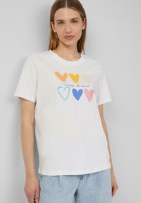 T-shirt en coton blanc présentant un graphique de cœurs colorés en orange, jaune, turquoise, bleu, rose, avec le texte "sois toujours gentil."