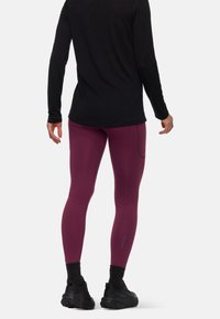 Mörkröda leggings med en figurnära design, med en sidficka. Kombineras med en svart långärmad topp och svarta sportskor.