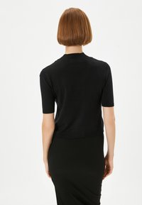 Sort kortærmet top med en tætsiddende design, ribbet halsudskæring og kant. Båret med en matchende sort ribbet nederdel, der fremviser en glat tekstur.