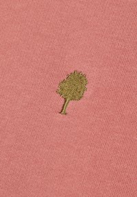 Piccolo albero ricamato di colore verde oliva su sfondo di tessuto rosa testurizzato.