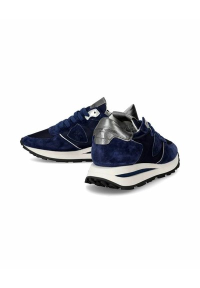 Marineblå ruskinds sneakers med metalisk sølvaccent, teksturerede sorte stofpaneler og en hvid mellemsål. Har en mønstret sål for godt greb.