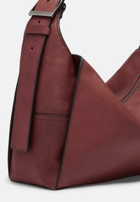 Borsa a spalla in pelle bordeaux con finitura testurizzata, forma geometrica, tracolla regolabile e dettaglio in metallo. Chiusura a zip visibile.