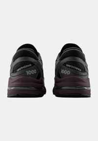 Svarta och grå träningsskor med en framträdande lila mellansula, mesh- och syntetiskt överdel, med stoppat stöd och "New Balance 1000"-logotyp.