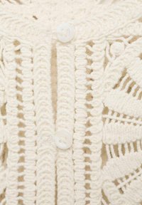 Lightweight cream knit cardigan with an open, lace-like design, featuring a round white button at the front and textured patterns.