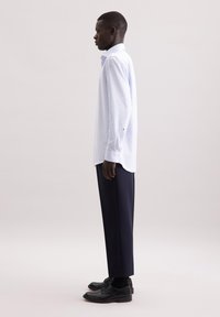 Camicia a quadri blu chiaro con colletto abbottonato, maniche lunghe e vestibilità dritta, abbinata a pantaloni blu navy e scarpe nere.