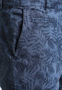 Mörkblå bomullsbyxor med ett subtilt mönster av ormbunkar. Har en sidficka och sydda detaljer. Slät textur och figurnära design.