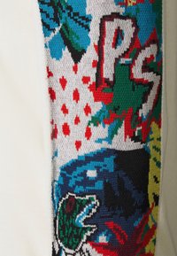 Panneau de tissu tricoté coloré sur fond crème présentant des formes abstraites, des feuilles bleues et vertes, des points rouges, et les lettres "PS".