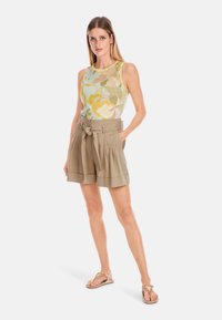 Floral tank top in light pastel colors and green accents, paired with beige high-waisted pleated shorts with a front belt tie. Flip-flops.