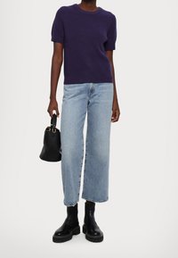 Fialový žebrovaný pletený svetr s krátkými rukávy, světle modré džínsy s širokými nohavicemi, černé kotníkové boty a malá černá kabelka.