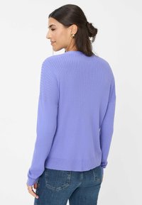 Lila, gerippter Pullover mit langen Ärmeln und Rundhalsausschnitt, der einen lockeren Schnitt und einen strukturierten Stoff aufweist; kombiniert mit blauen Jeans.