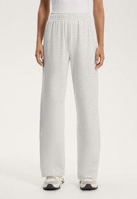 Svetlo sivi trenirka s sproščenim krojem, elastičnim pasom in mehkimi vlakni. V kombinaciji z športnimi čevlji nevtralnih tonov.